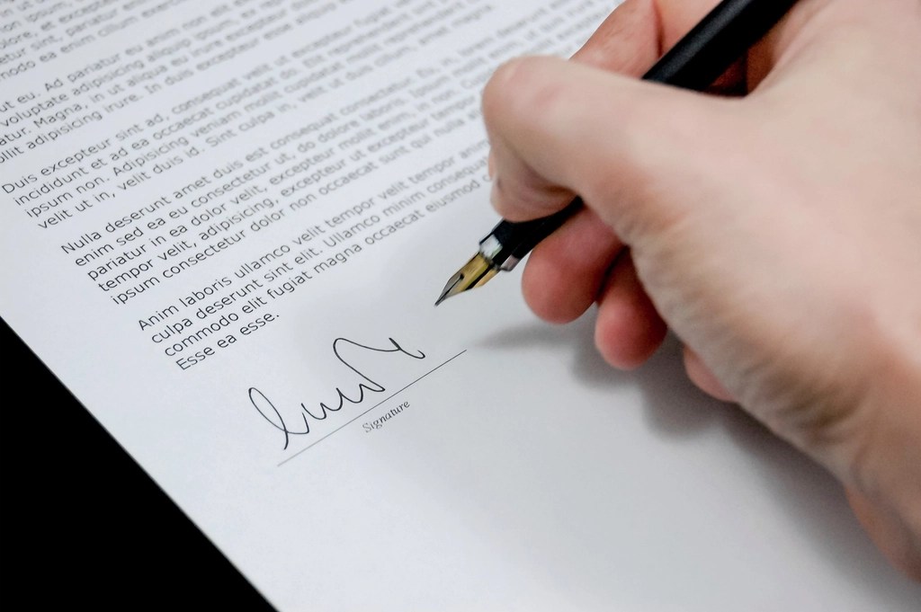 A hand signing a document with a pen